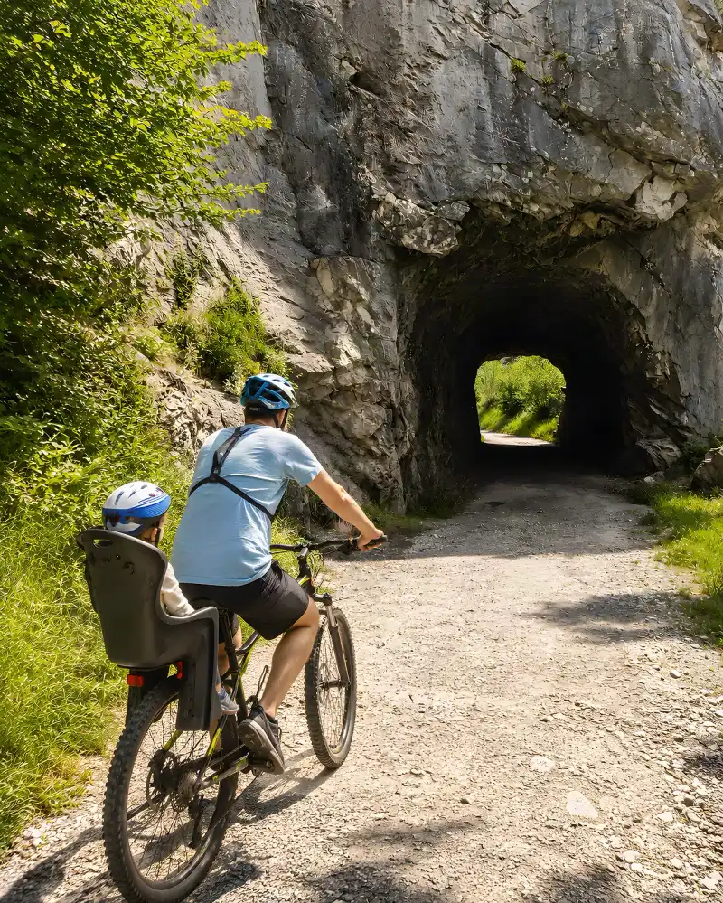 Padre en bici con su hijo en la sillita infantil ante uno de los túneles de la Ruta del Oso